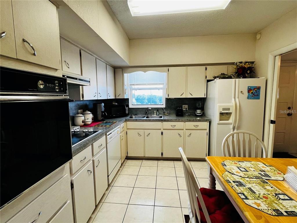 A kitchen with white cabinets, tile flooring, a dining table, and white appliances — 2340 GRECIAN WAY UNIT 56, CLEARWATER, FL