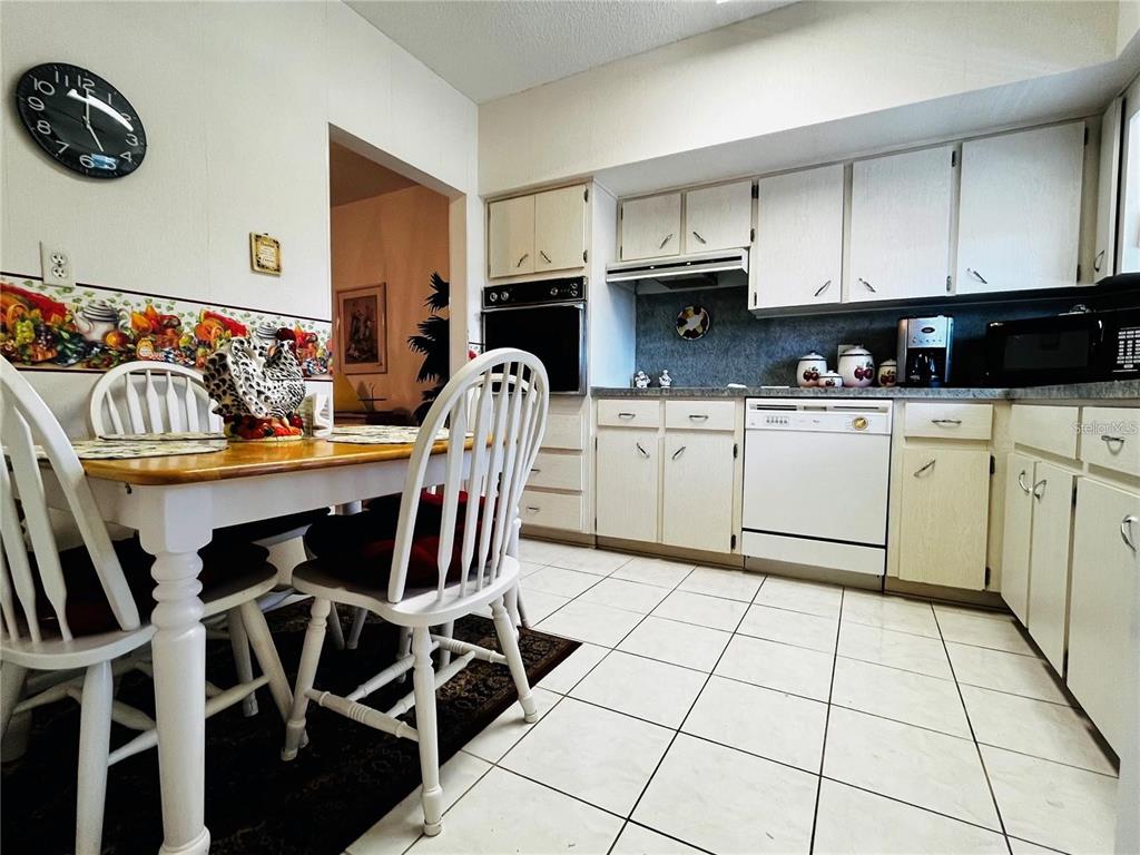 A kitchen features white cabinets, a dining table with chairs, and tiled flooring — 2340 GRECIAN WAY UNIT 56, CLEARWATER, FL