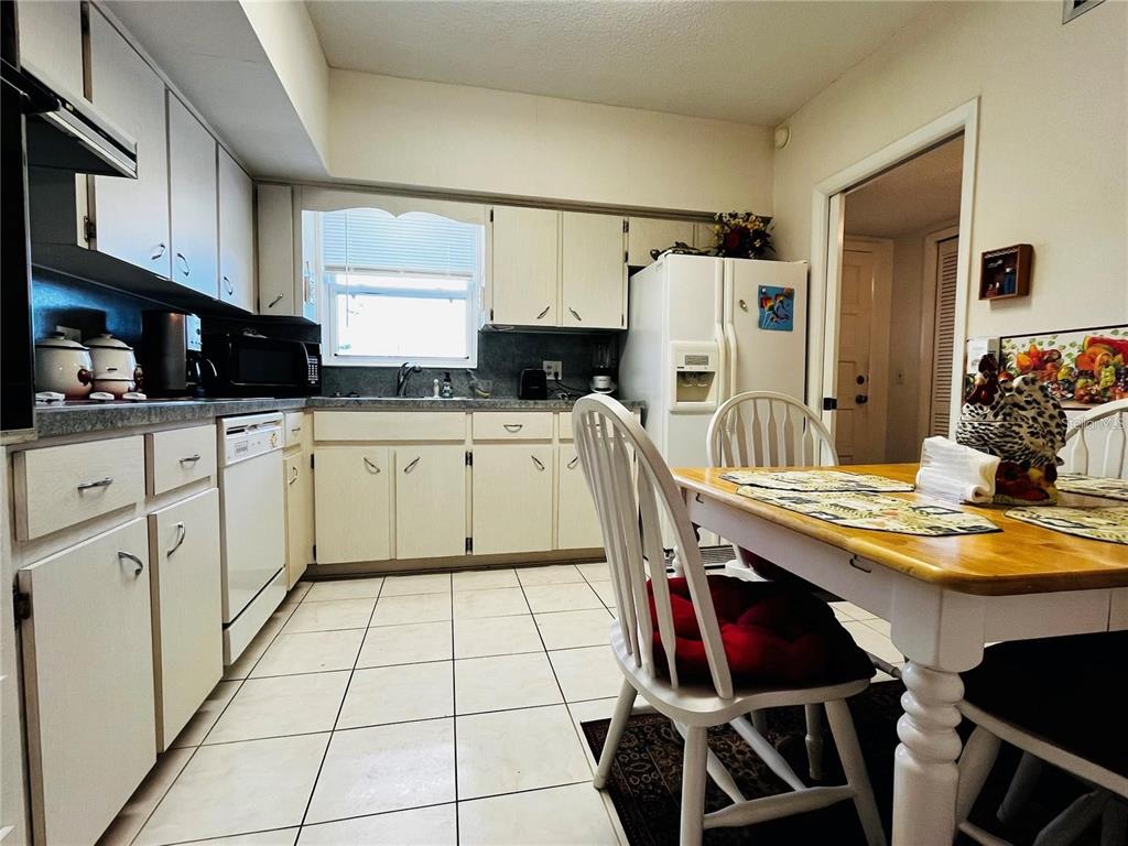 A kitchen with white cabinets, tile flooring, and a wooden dining table with chairs — 2340 GRECIAN WAY UNIT 56, CLEARWATER, FL