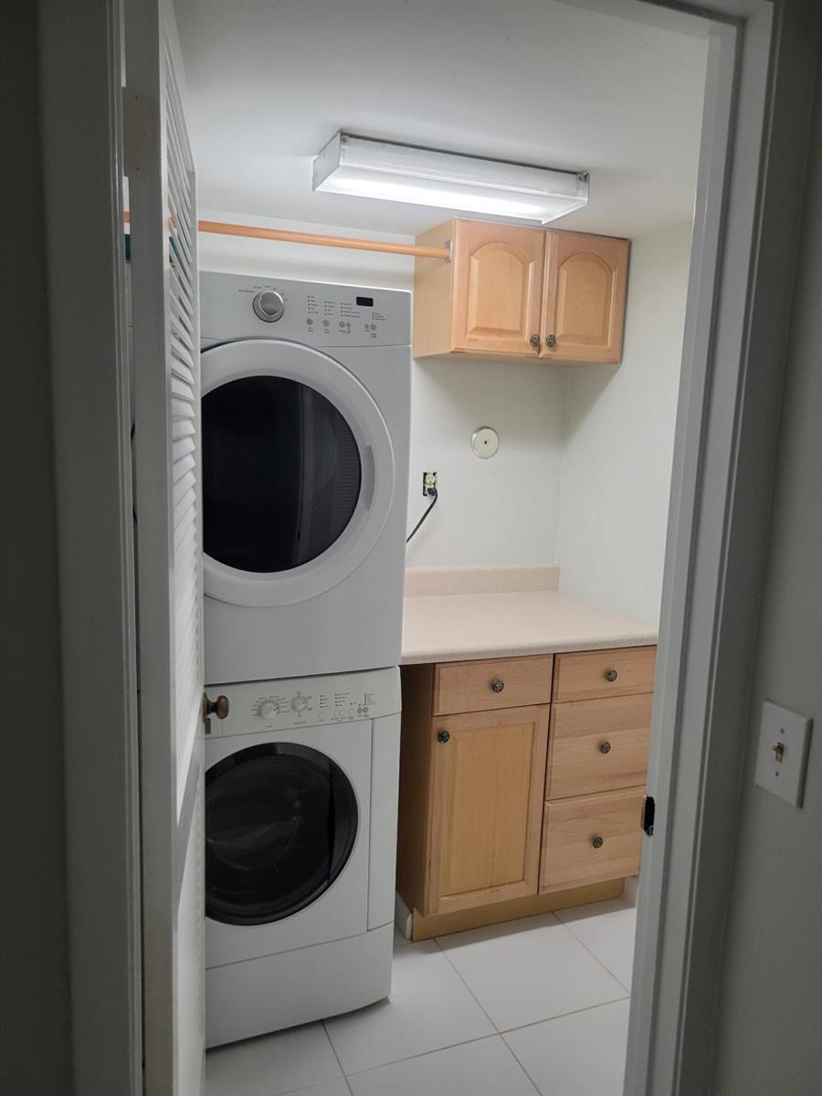A laundry room featuring a stacked washer and dryer, wooden cabinetry, and a countertop — 3345 Perimeter Drive # 1311, FL 33467, FL