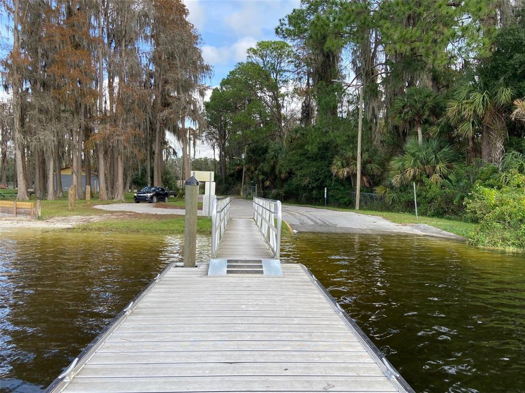 A wooden boat dock leads to a paved boat ramp surrounded by trees and water — 9260 LAKE DRIVE, NEW PORT RICHEY, FL