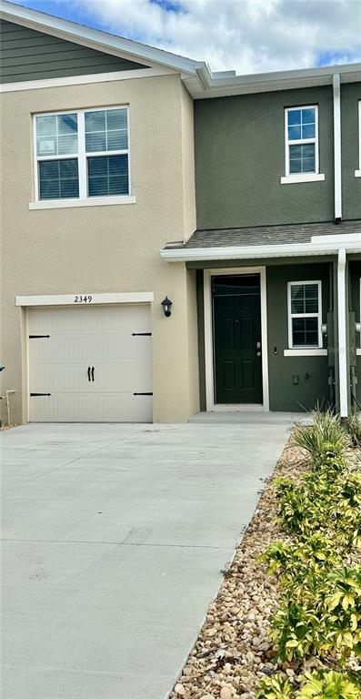 A two-story townhouse exterior features a beige garage, a dark green front door, and a driveway — 2349 PENGUIN BOULEVARD, DAVENPORT, FL