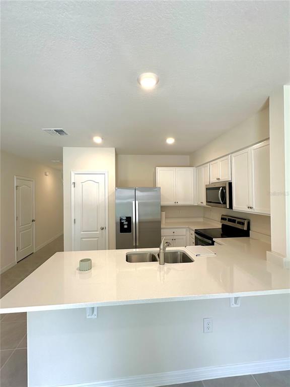 A kitchen features white cabinets, stainless steel appliances, and a white quartz breakfast bar — 2349 PENGUIN BOULEVARD, DAVENPORT, FL