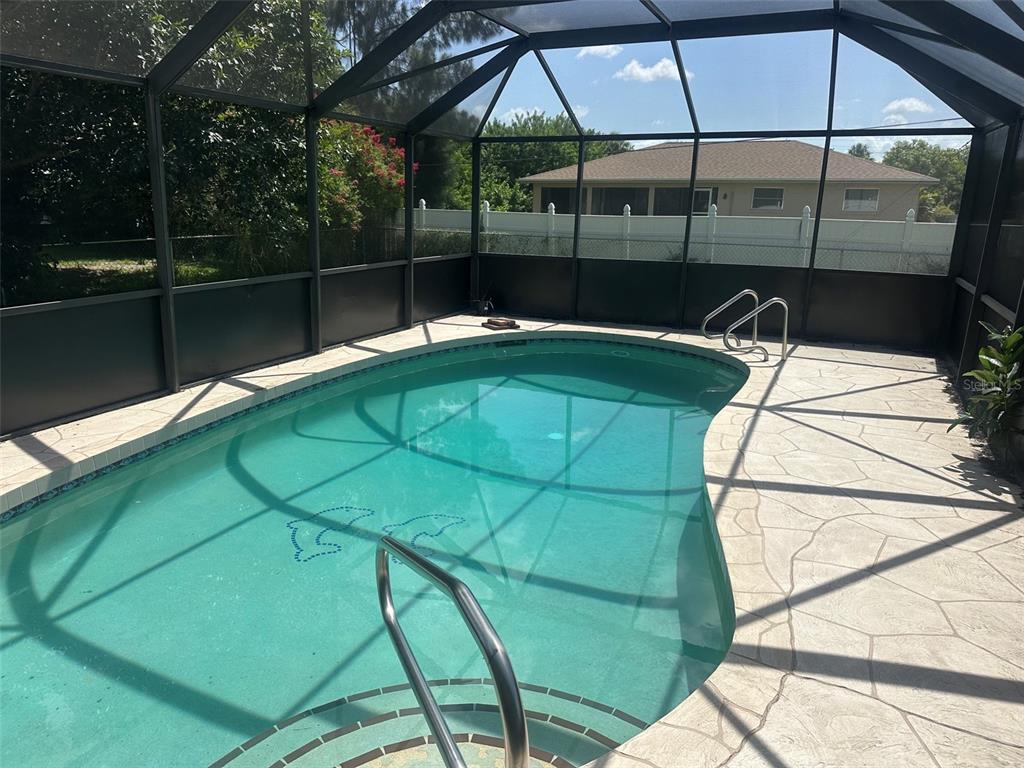 A kidney-shaped swimming pool is enclosed by a screened lanai with a concrete patio — 4222 COCKRELL STREET, PORT CHARLOTTE, FL