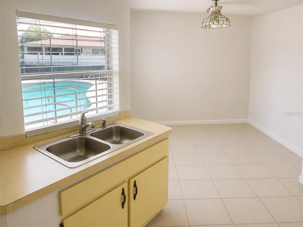 A kitchen sink with yellow cabinets overlooks a backyard swimming pool through a window — 4222 COCKRELL STREET, PORT CHARLOTTE, FL
