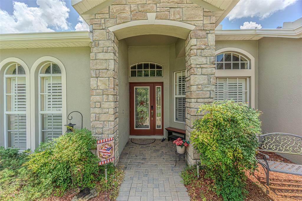 The exterior entrance features a stone-faced archway, a red front door, and a brick walkway — 10404 BELMULLET DRIVE, SAN ANTONIO, FL