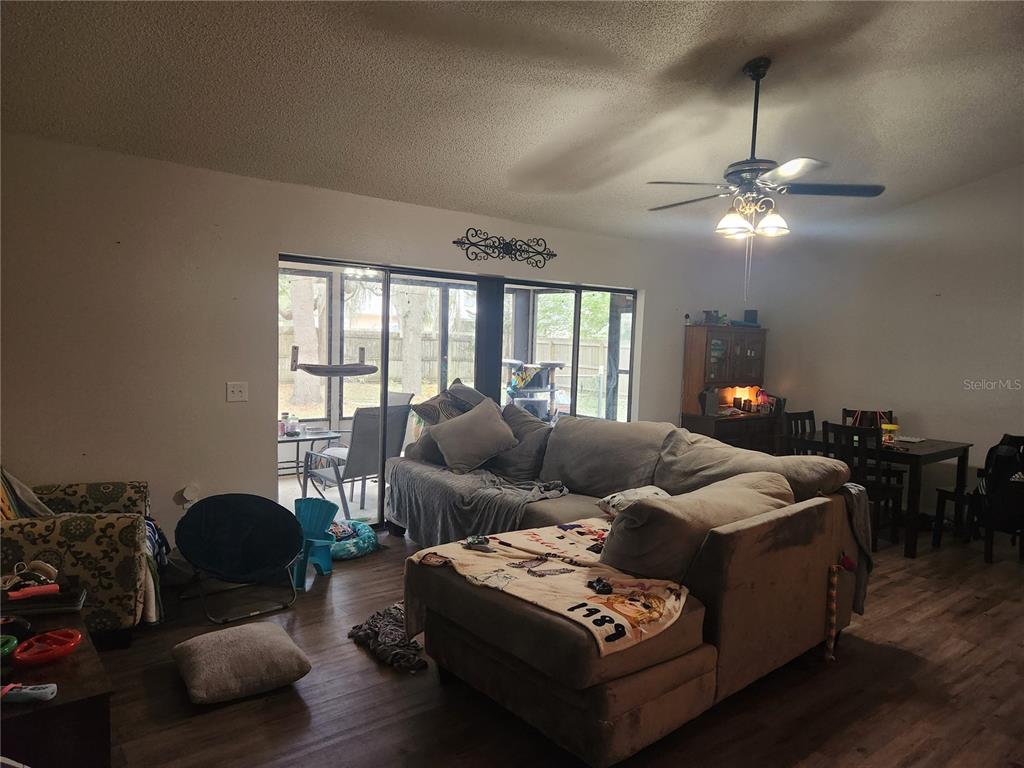 A living room with wood-look flooring, a large sectional sofa, and sliding glass doors — 6202 PIEDMONT DRIVE, SPRING HILL, FL