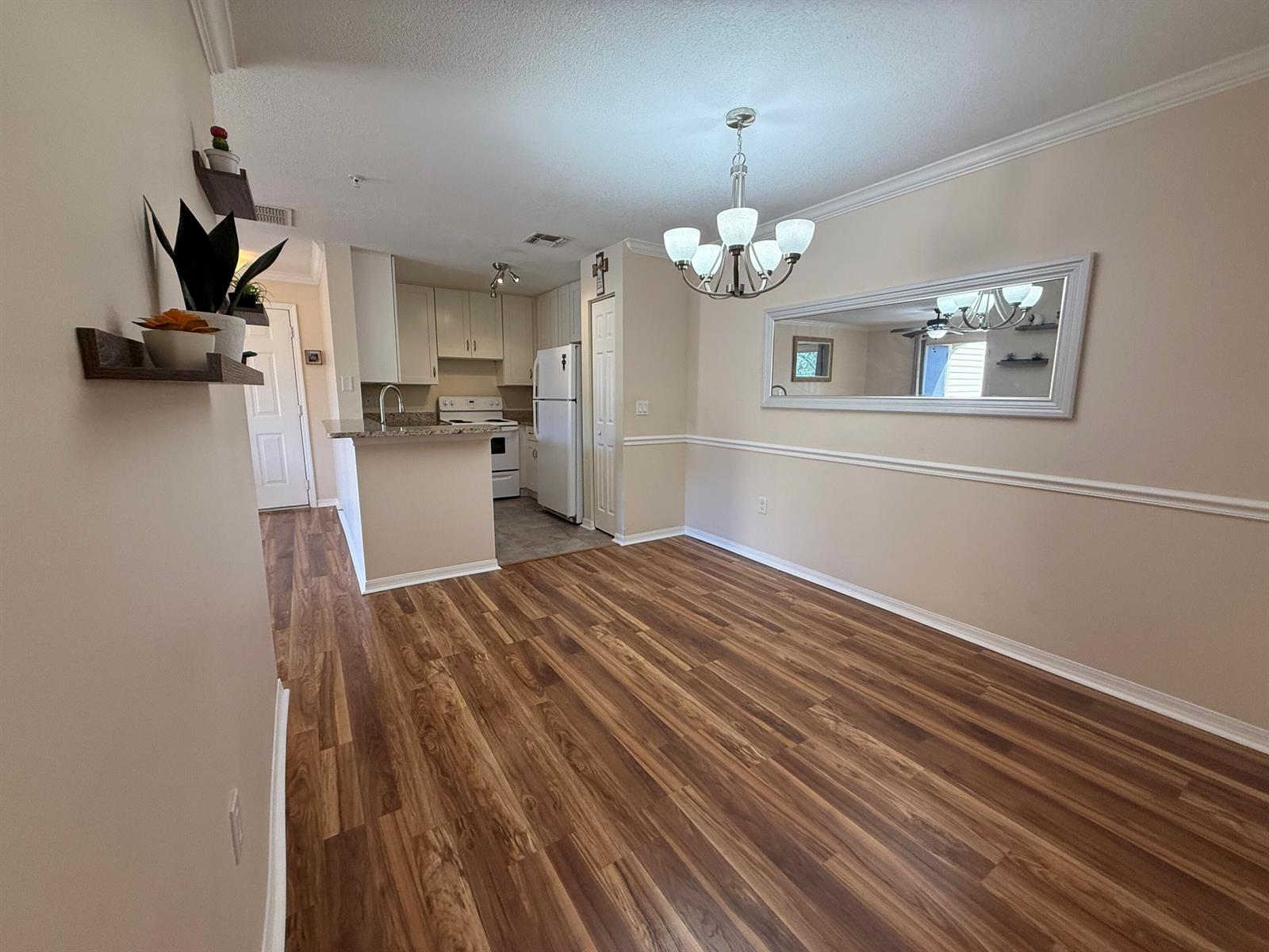 A dining area with wood-look flooring, a chandelier, and a large mirror leads to a kitchen — 1979 Summer Club Drive # 213, FL 32765, FL