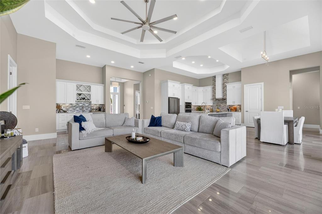 An open-concept living room and kitchen featuring tray ceilings, gray tile floors, and white cabinetry — 638 MANNS HARBOR DRIVE, APOLLO BEACH, FL