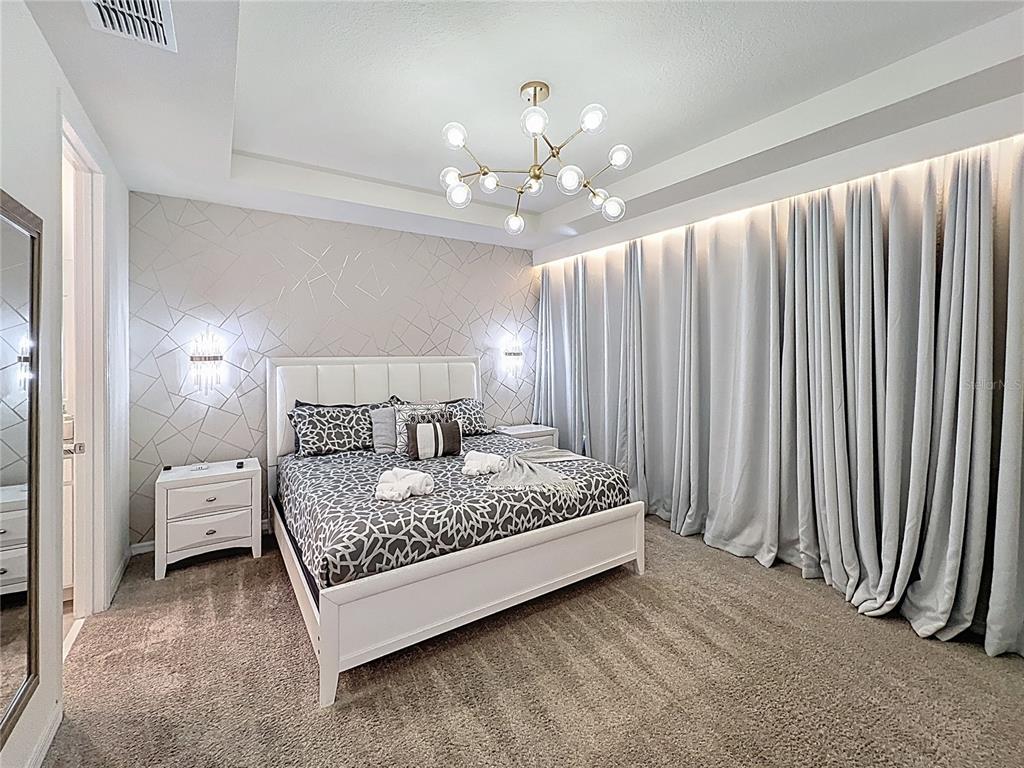 A bedroom features a white bed, patterned bedding, geometric wallpaper, and floor-to-ceiling curtains — 1800 TROPICAL PALMS CIRCLE, KISSIMMEE, FL
