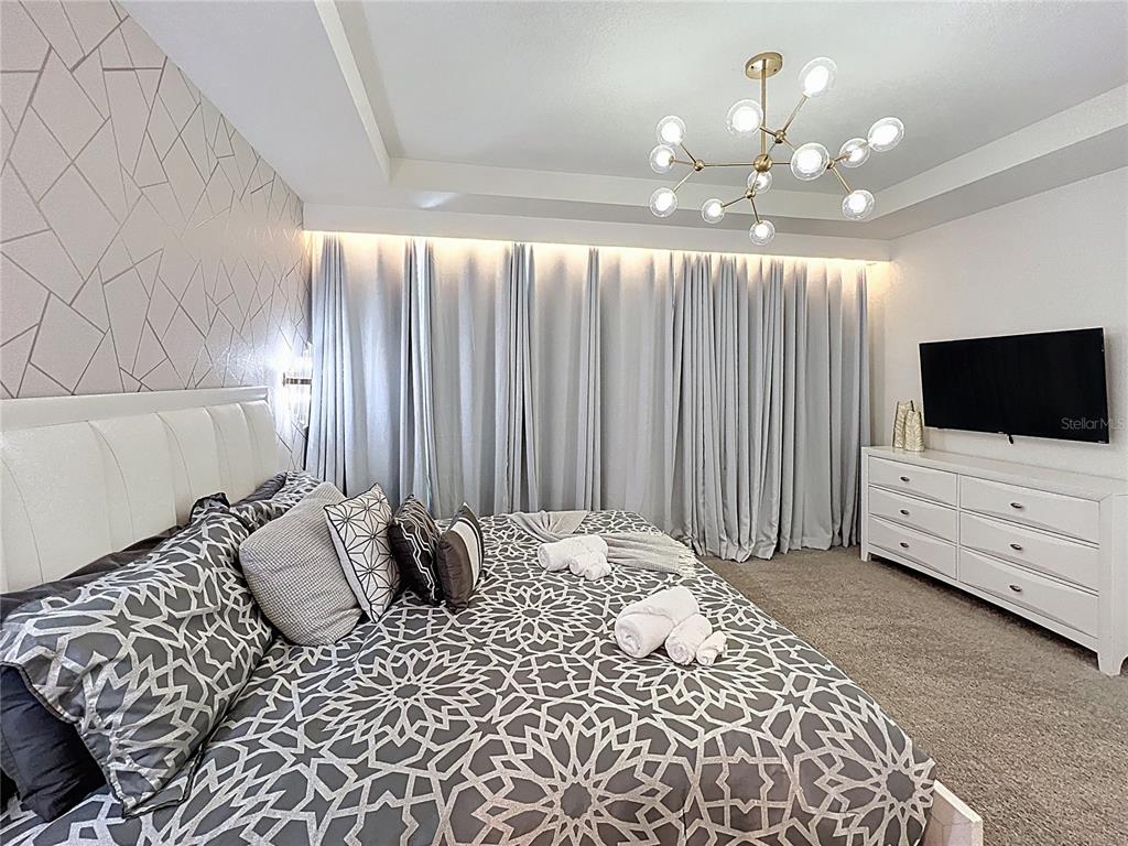 A bedroom features a patterned accent wall, a modern chandelier, and a large bed — 1800 TROPICAL PALMS CIRCLE, KISSIMMEE, FL