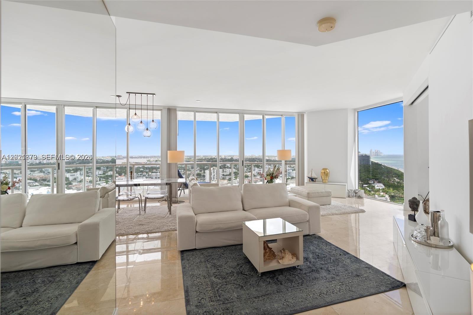 A bright living and dining area features white furniture, marble floors, and floor-to-ceiling windows — 7330 Ocean Ter # D, Miami Beach FL 33141, MIAMI BEACH, FL