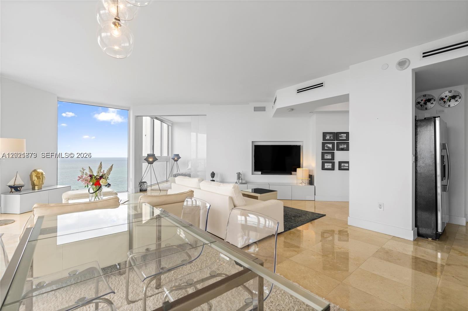 A bright living and dining area features white furniture, a glass table, and ocean views — 7330 Ocean Ter # D, Miami Beach FL 33141, MIAMI BEACH, FL