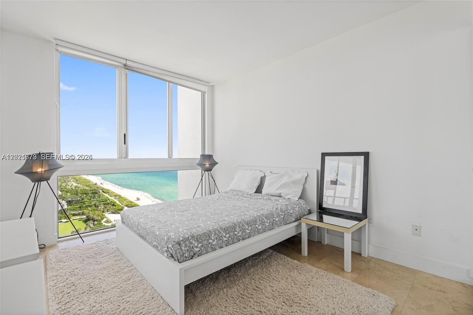 A bedroom features a bed, a floor lamp, and a large window overlooking the ocean — 7330 Ocean Ter # D, Miami Beach FL 33141, MIAMI BEACH, FL