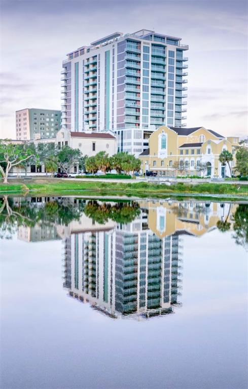 A tall modern apartment building and a historic yellow building reflect in a calm lake — 777 3RD AVENUE N UNIT 1603, ST PETERSBURG, FL