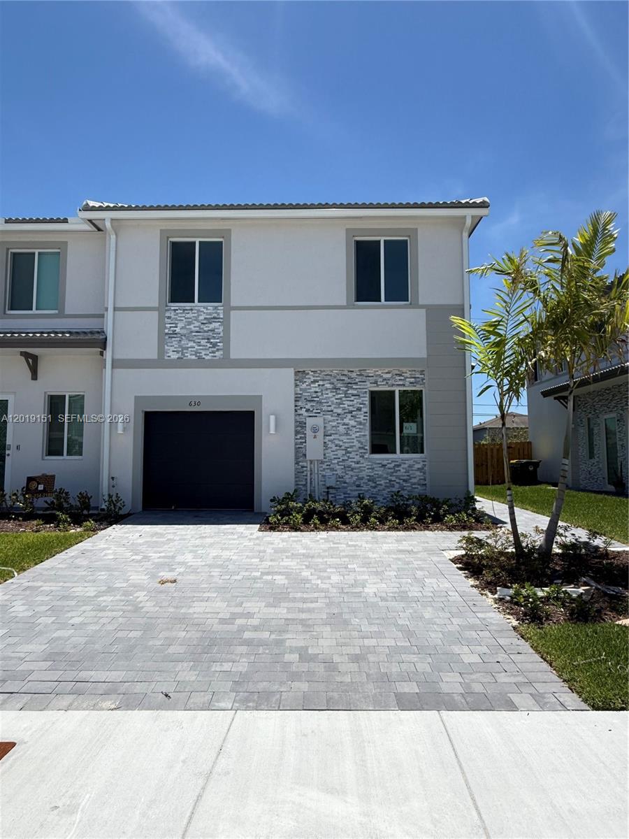 A two-story townhouse with a stone-accented facade, a paved driveway, and a single-car garage — 630 SE 15th St # 630, Homestead FL 33034, HOMESTEAD, FL