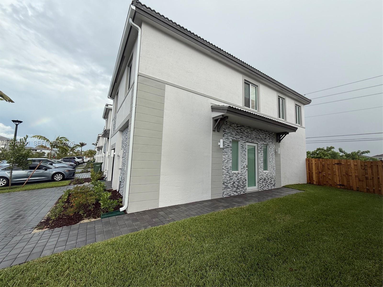 A two-story townhouse exterior features white stucco, gray accents, and a stone-veneer entryway — 630 SE 15th St # 630, Homestead FL 33034, HOMESTEAD, FL