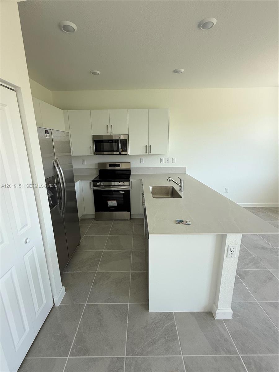 A modern kitchen features white cabinetry, stainless steel appliances, and a large quartz island — 630 SE 15th St # 630, Homestead FL 33034, HOMESTEAD, FL