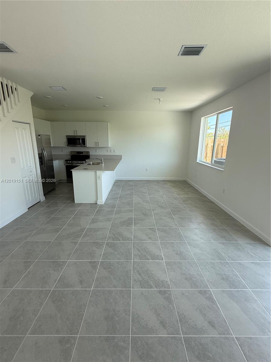 An open-concept kitchen and living area features white cabinetry, stainless steel appliances, and gray tile — 630 SE 15th St # 630, Homestead FL 33034, HOMESTEAD, FL
