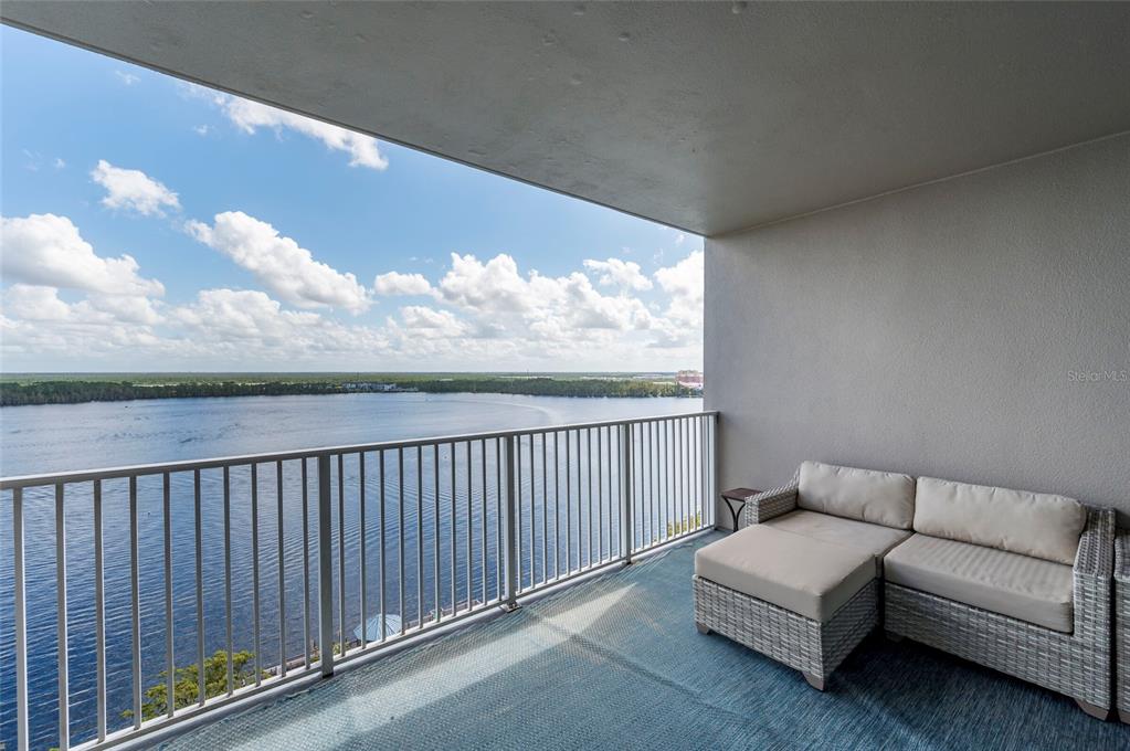 A balcony with a white wicker sectional sofa overlooks a large body of water — 13415 BLUE HERON BEACH DRIVE UNIT 1404, ORLANDO, FL