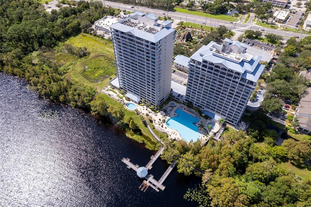 An aerial view shows two high-rise buildings beside a lake with a pool and dock — 13415 BLUE HERON BEACH DRIVE UNIT 1404, ORLANDO, FL