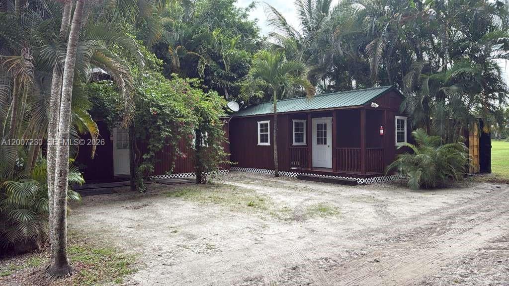 A brown wooden cabin with a green metal roof sits on a sandy lot — 14996 50th St S, Wellington FL 33414, WELLINGTON, FL