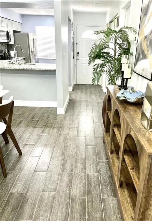 A hallway with wood-look tile flooring leads toward a white front door and kitchen area — 494 PRESTWICK PLACE UNIT N/A, KISSIMMEE, FL
