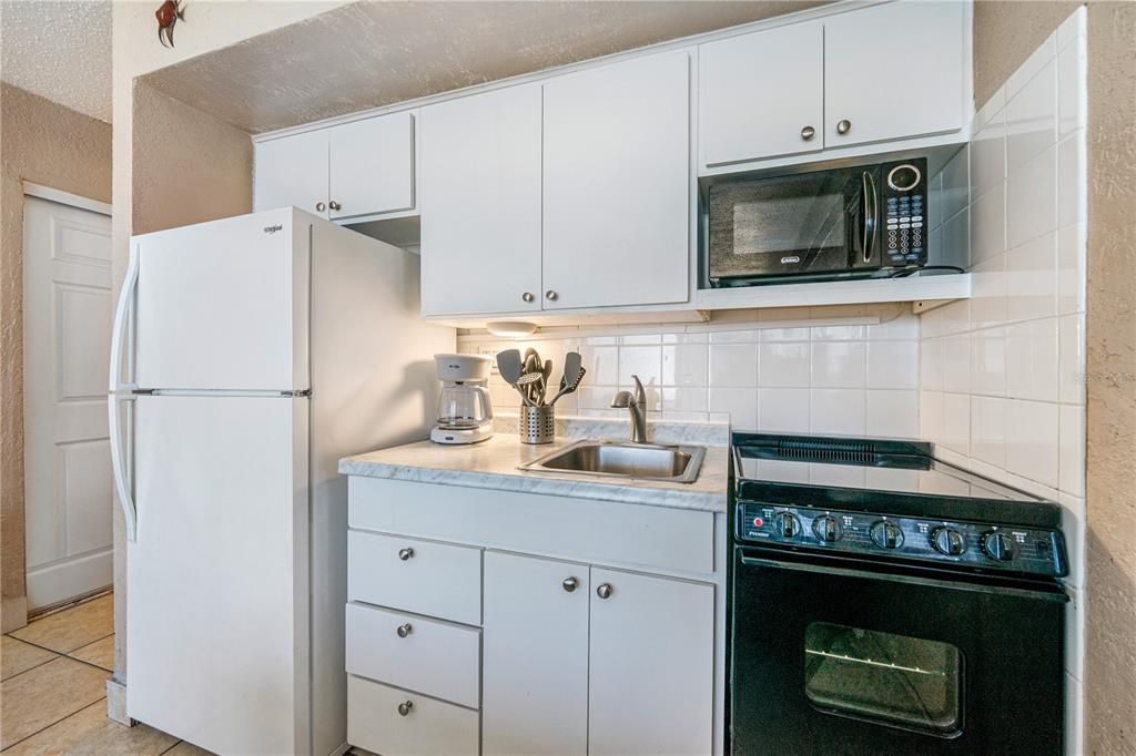 A small kitchen features white cabinets, a white refrigerator, a black stove, and a microwave — 2301 S ATLANTIC AVENUE UNIT 338, DAYTONA BEACH, FL