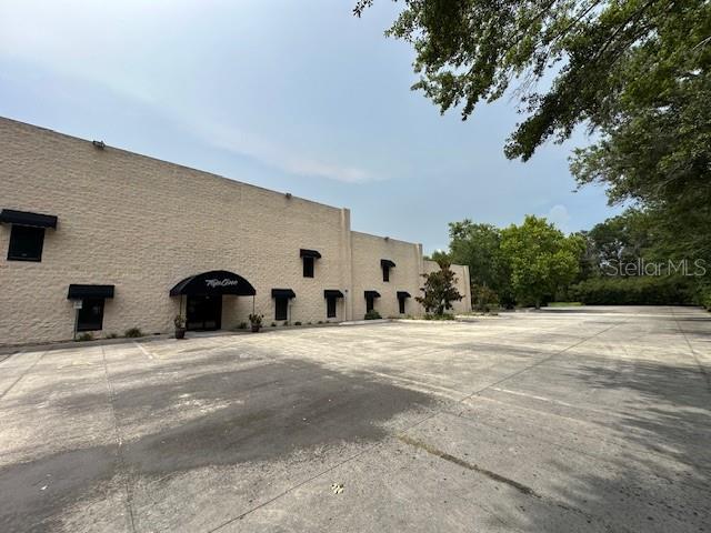 A beige commercial building with black awnings sits beside a large, empty concrete parking lot — 2251 TOPLINE WAY UNIT 4, BROOKSVILLE, FL
