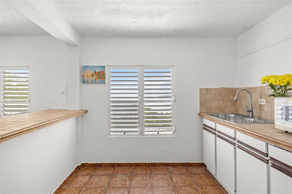 A kitchen features white cabinets, tiled countertops, a double sink, and louvered windows — 39 COMM PLAYA GUAYANES, YABUCOA, PR