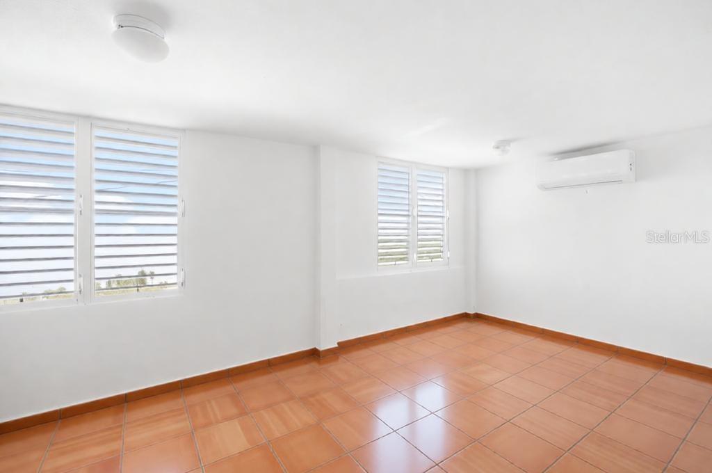An empty room with white walls, tile flooring, louvered windows, and a wall-mounted air conditioner — 39 COMM PLAYA GUAYANES, YABUCOA, PR
