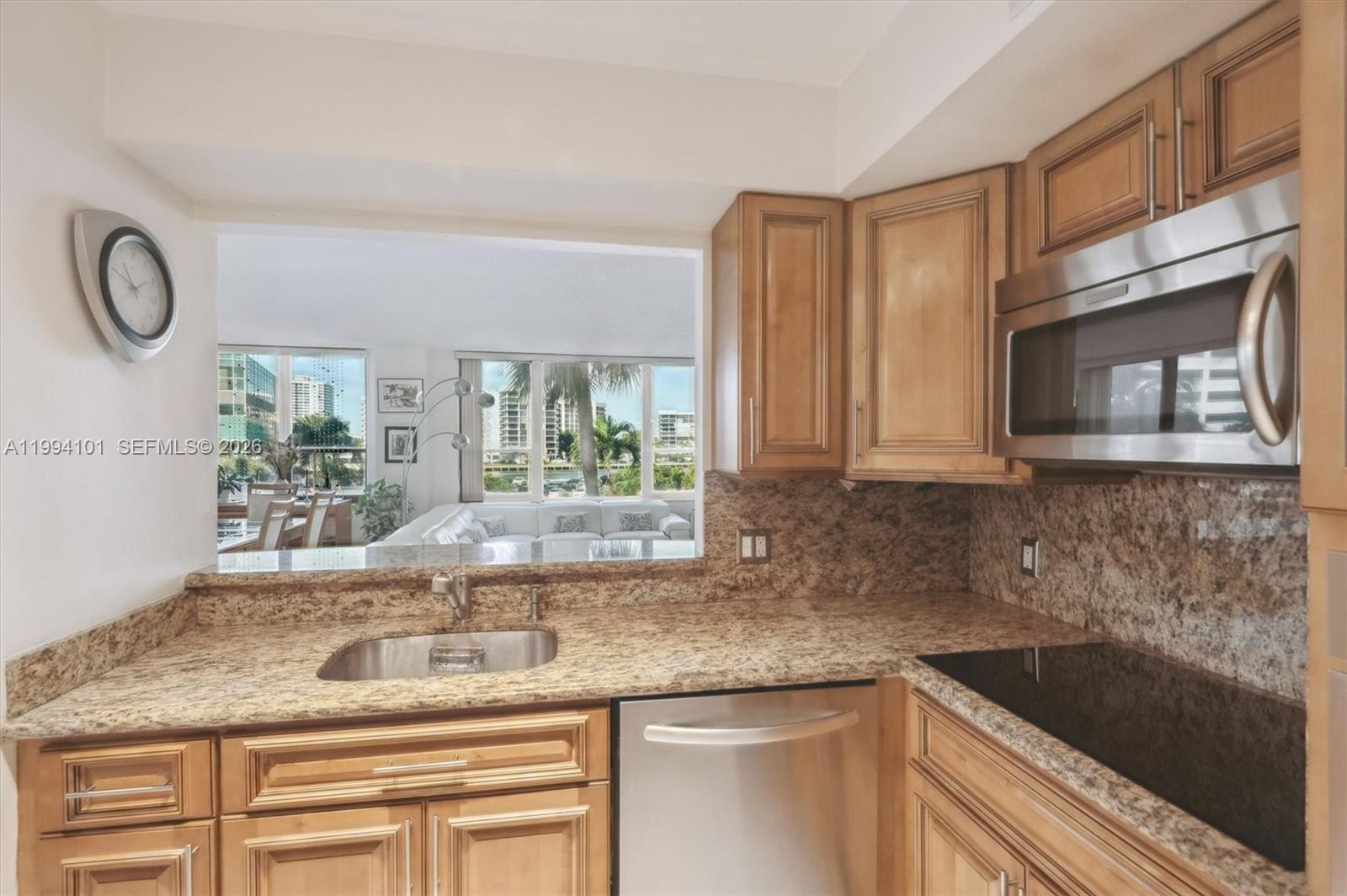 A kitchen features granite countertops, light wood cabinets, stainless steel appliances, and a pass-through window — 3505 S Ocean Dr # 201, Hollywood FL 33019, HOLLYWOOD, FL