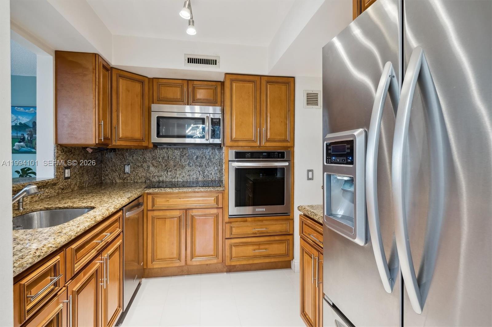 A kitchen features wood cabinets, granite countertops, stainless steel appliances, and white tile flooring — 3505 S Ocean Dr # 201, Hollywood FL 33019, HOLLYWOOD, FL