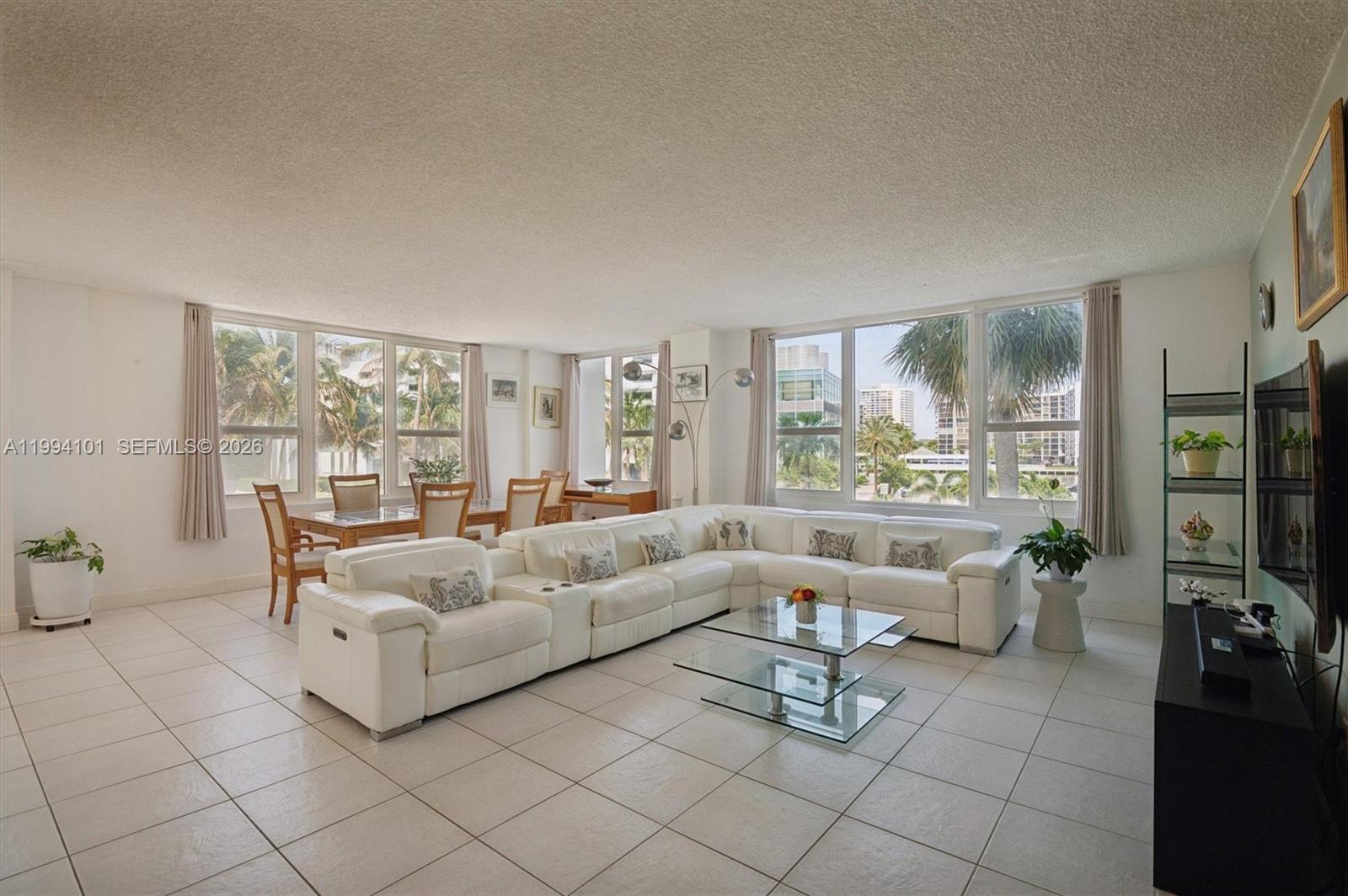 A bright living and dining room features white tile floors, a sectional sofa, and windows — 3505 S Ocean Dr # 201, Hollywood FL 33019, HOLLYWOOD, FL