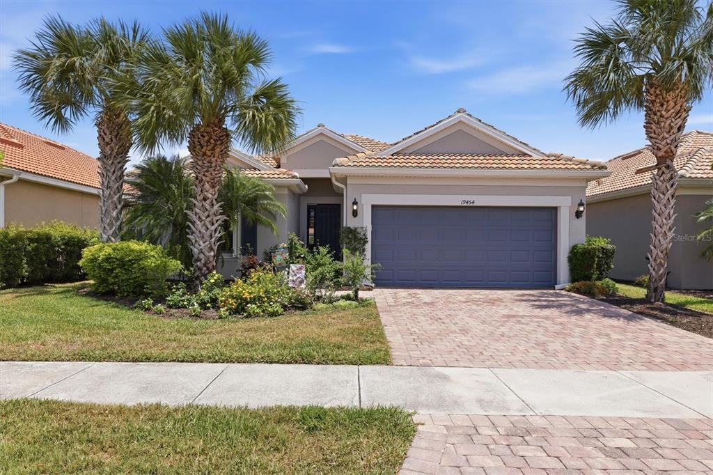 A single-story house with a blue garage door, palm trees, and a brick paver driveway — 19454 RIZZUTO STREET, VENICE, FL