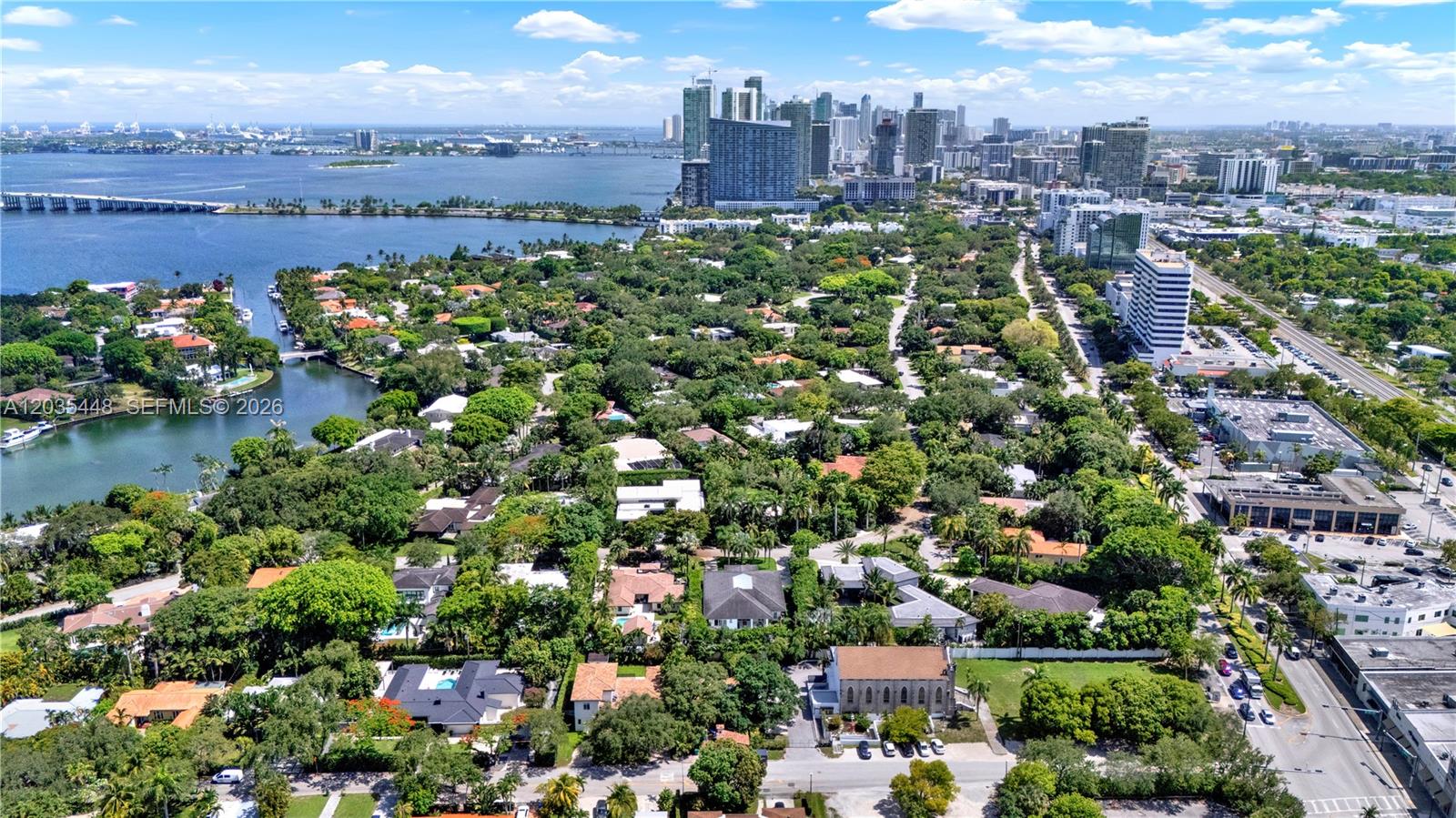 An aerial view shows a lush residential neighborhood near a bay with a city skyline — 520 Bay Point Rd, Miami FL 33137, MIAMI, FL