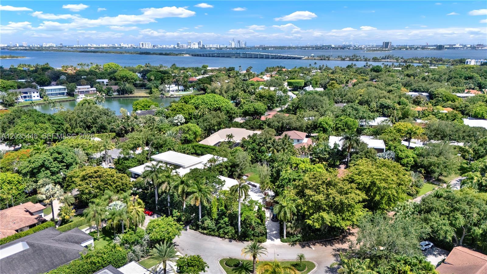 An aerial view shows a lush, tree-filled residential neighborhood near a bay and bridge — 520 Bay Point Rd, Miami FL 33137, MIAMI, FL