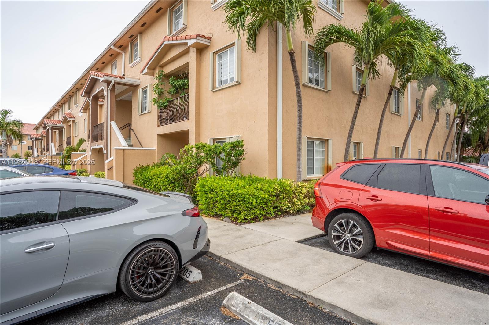 The exterior of a multi-story tan apartment building features palm trees and parked cars — 17425 NW 75th Pl # 101, Hialeah FL 33015, HIALEAH, FL