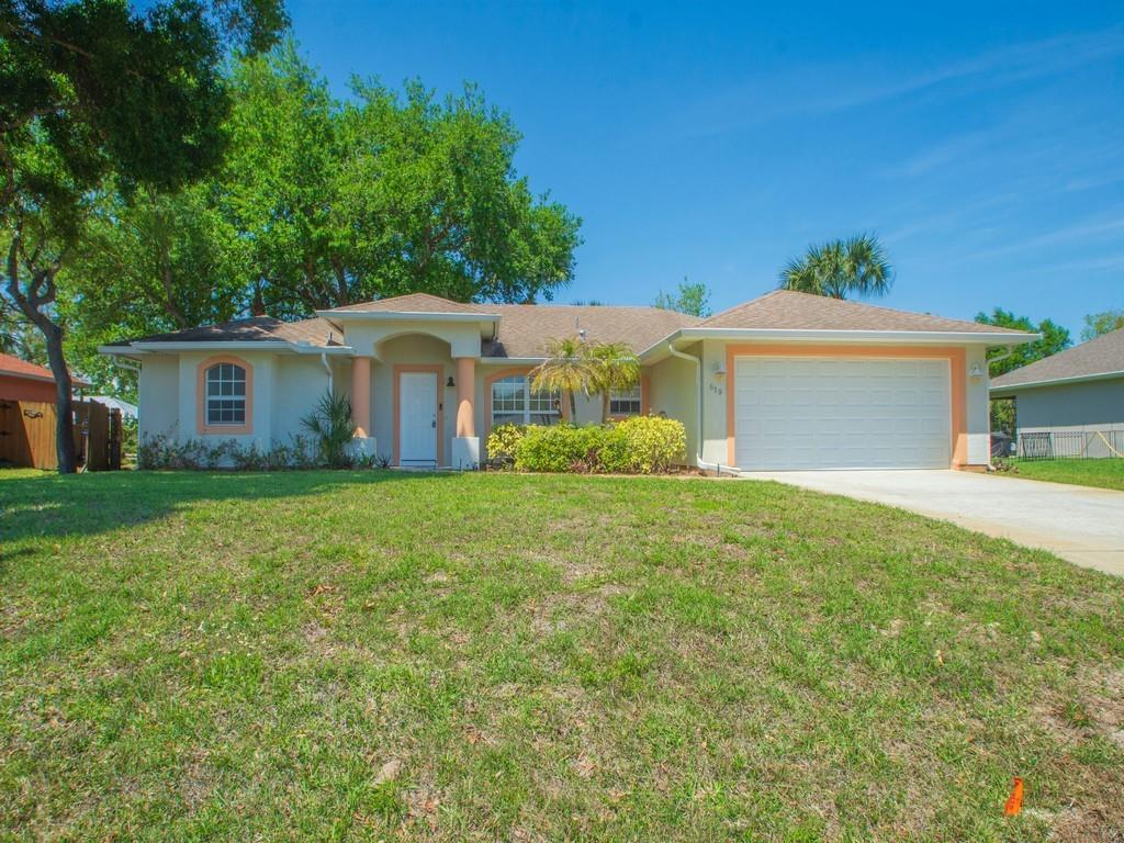 A single-story house with a white garage, tan stucco exterior, and a green lawn — 619 Carnival Terrace, Sebastian FL 32958, SEBASTIAN, FL