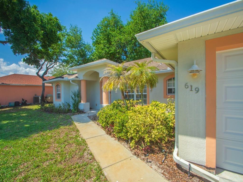 A single-story house with a beige stucco exterior, orange trim, and a concrete walkway — 619 Carnival Terrace, Sebastian FL 32958, SEBASTIAN, FL