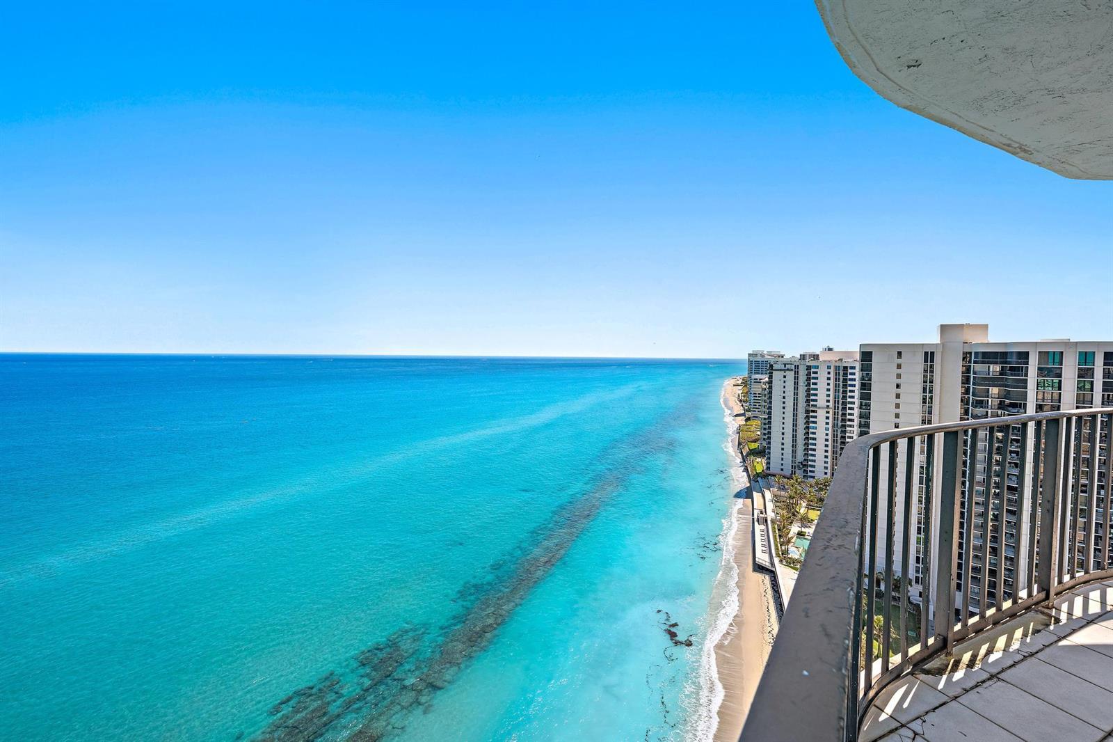 A high-angle view from a balcony overlooking a beach, the ocean, and nearby high-rise buildings — 5420 N Ocean Drive, Riviera Beach FL 33404, RIVIERA BEACH, FL
