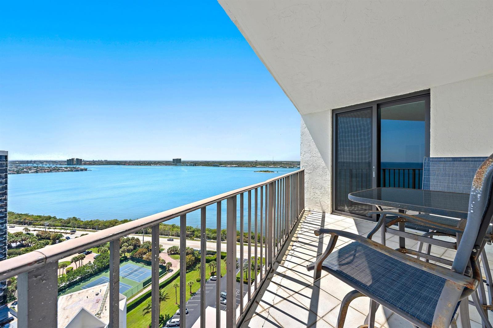 A high-rise balcony features metal furniture overlooking a large bay and tennis courts below — 5420 N Ocean Drive, Riviera Beach FL 33404, RIVIERA BEACH, FL