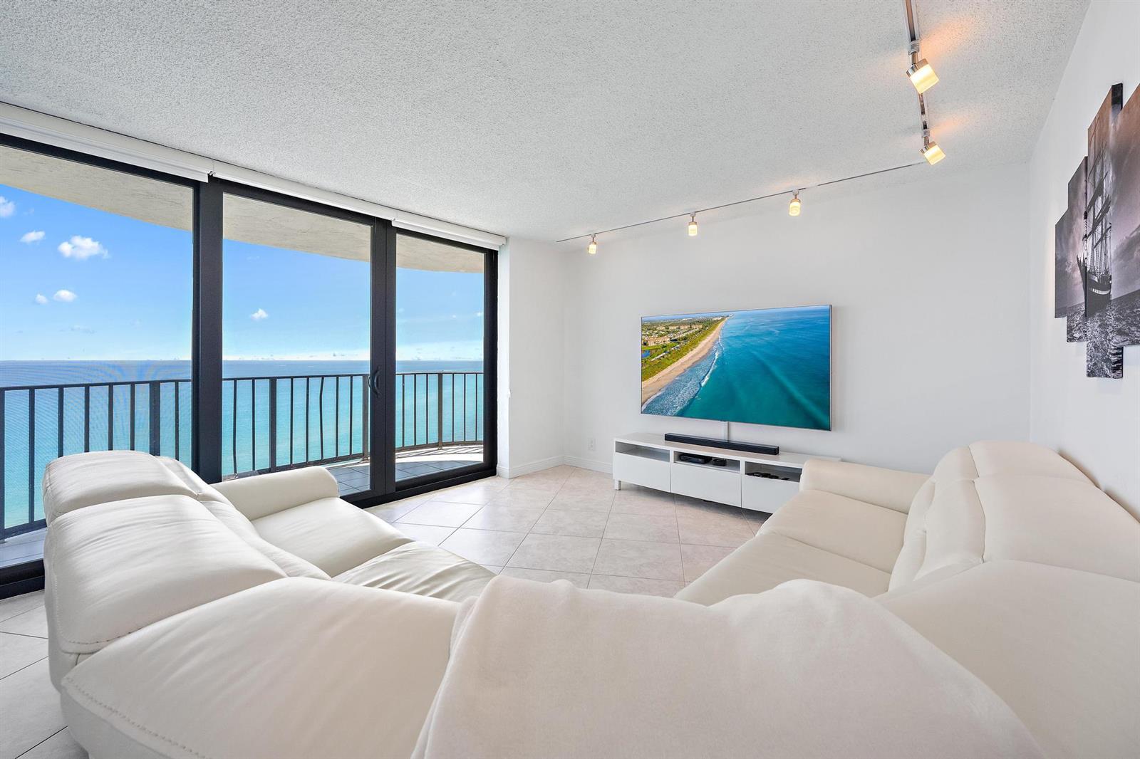 A living room features a white sectional sofa, a wall-mounted television, and a balcony view — 5420 N Ocean Drive, Riviera Beach FL 33404, RIVIERA BEACH, FL