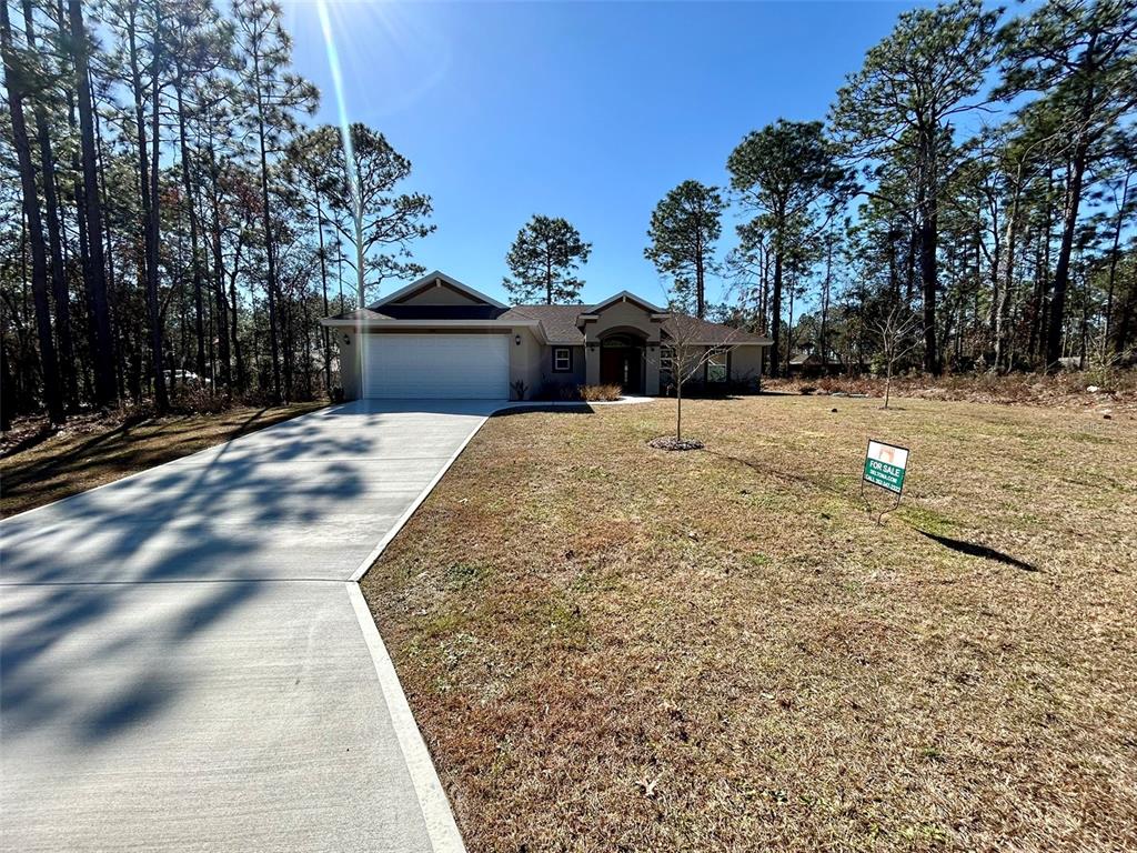A single-story house with a white garage door and a concrete driveway sits among trees — 1510 W GAINSBORO LANE, CITRUS SPRINGS, FL
