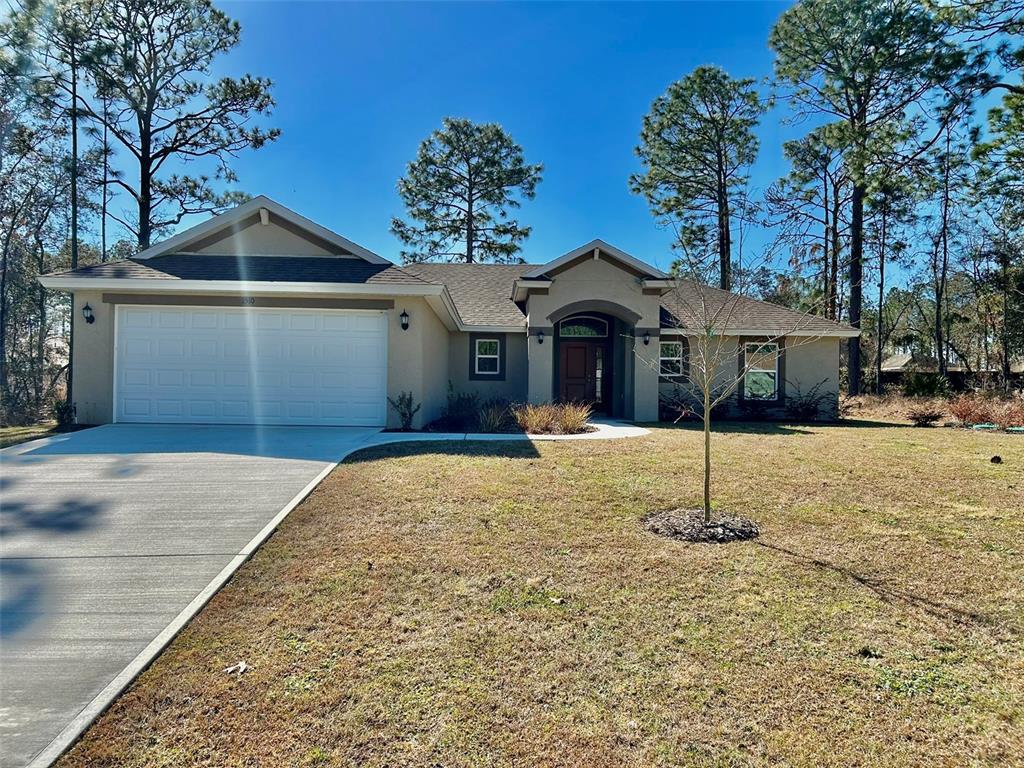 A single-story house with a two-car garage, tan stucco exterior, and a front entryway — 1510 W GAINSBORO LANE, CITRUS SPRINGS, FL