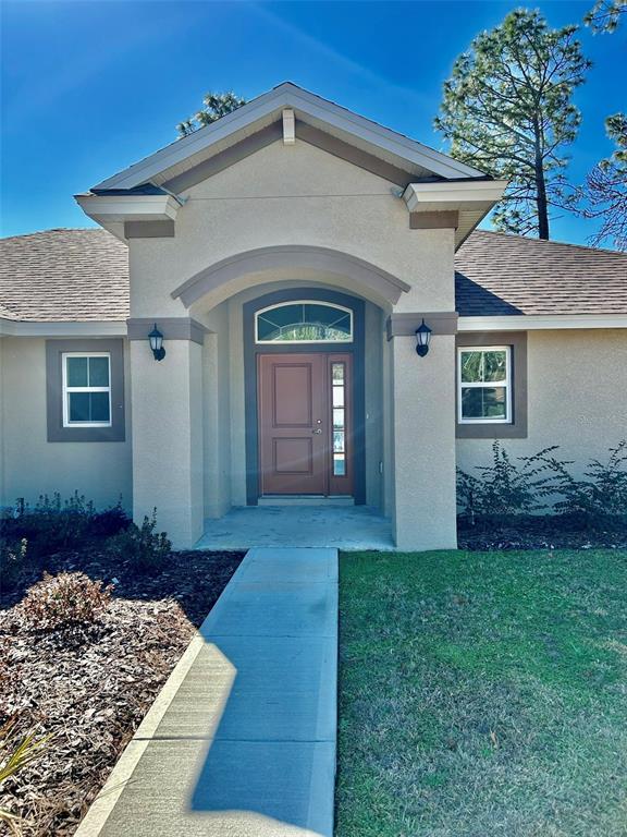 The exterior of a beige house features a covered entryway with a brown front door — 1510 W GAINSBORO LANE, CITRUS SPRINGS, FL