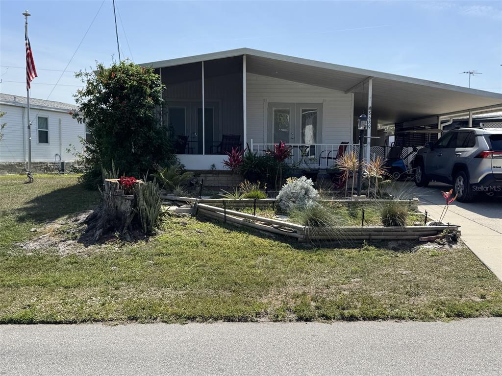 A single-story mobile home features a screened-in porch, a carport, and a landscaped front yard — 8689 BREEZE HILL DRIVE, LAKE WALES, FL