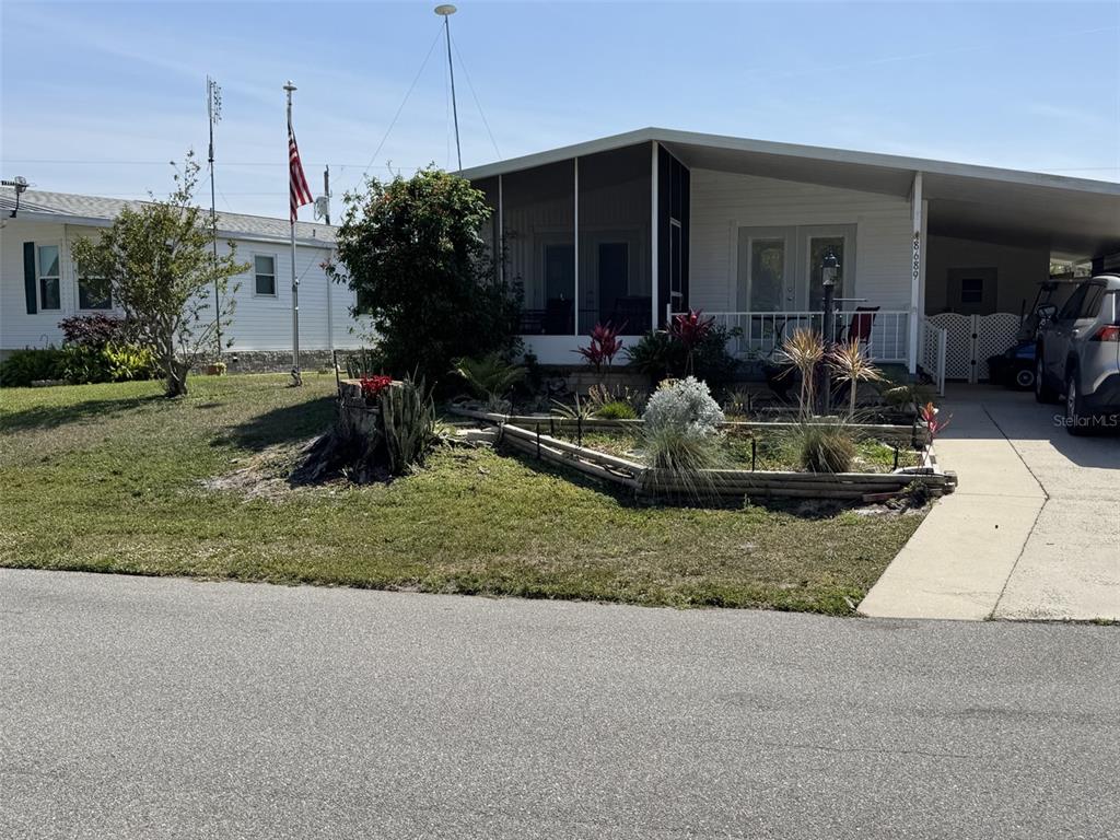 A single-story manufactured home features a screened-in porch, a carport, and a landscaped front yard — 8689 BREEZE HILL DRIVE, LAKE WALES, FL