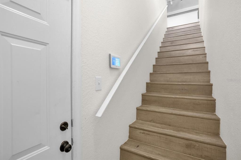 A white door stands next to a wooden staircase with a wall-mounted smart home panel — 845 GRAND REGENCY POINT UNIT 203, ALTAMONTE SPRINGS, FL