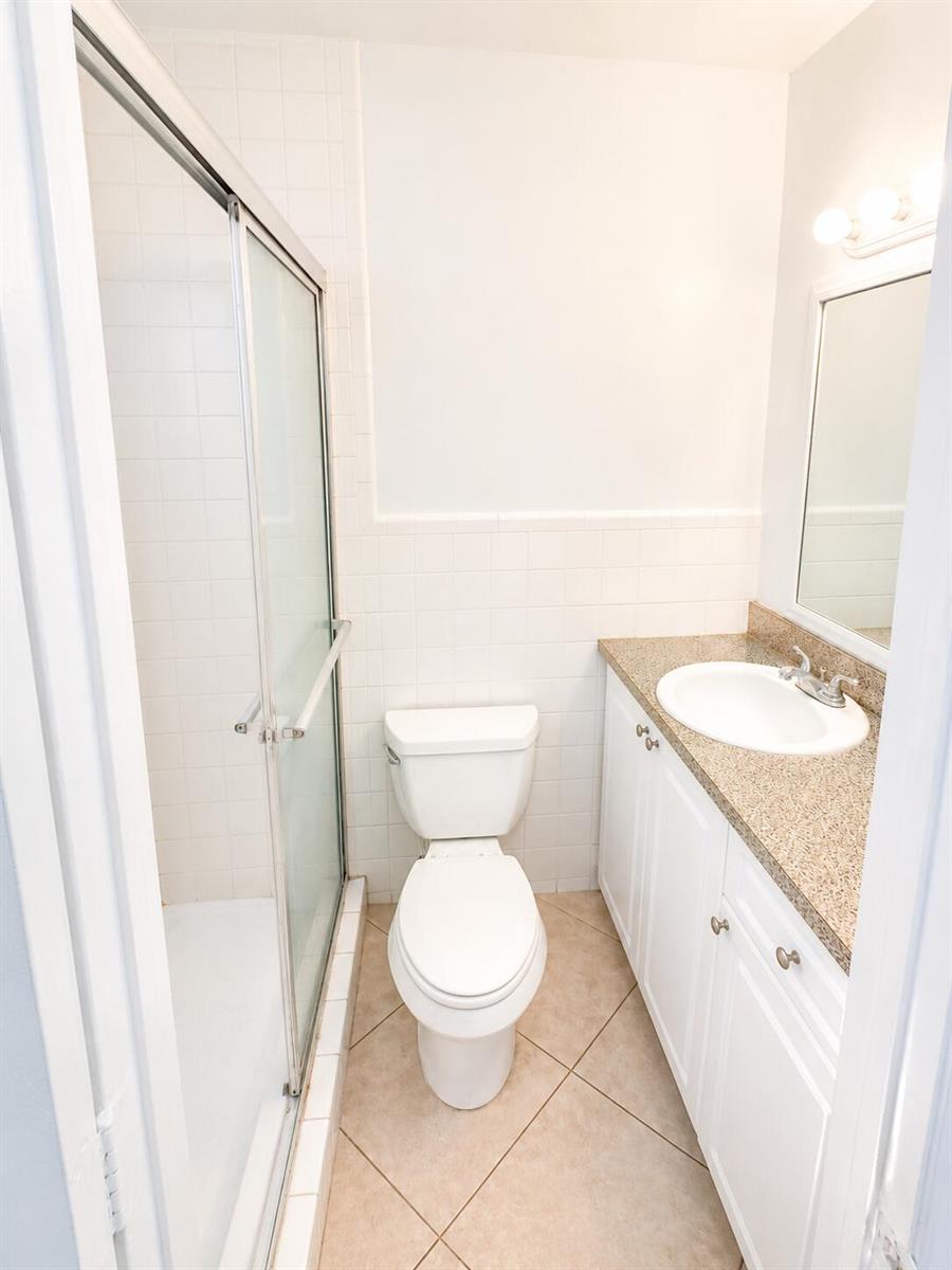 A bathroom features a glass-enclosed shower, a white toilet, and a vanity with a stone countertop — 1960 NE 48th Street # 7, Pompano Beach FL 33064, POMPANO BEACH, FL